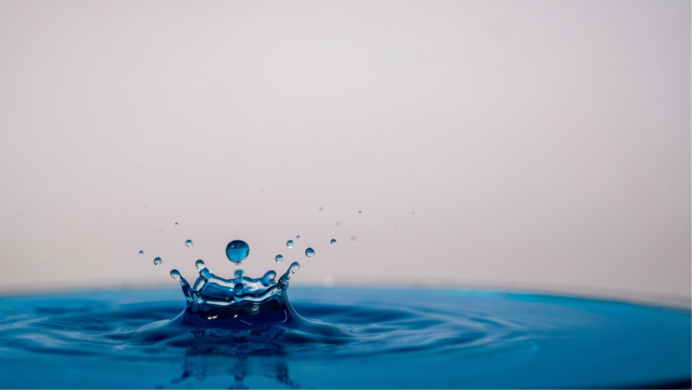 Water droplet creating ripples on a blue surface with a light gray background